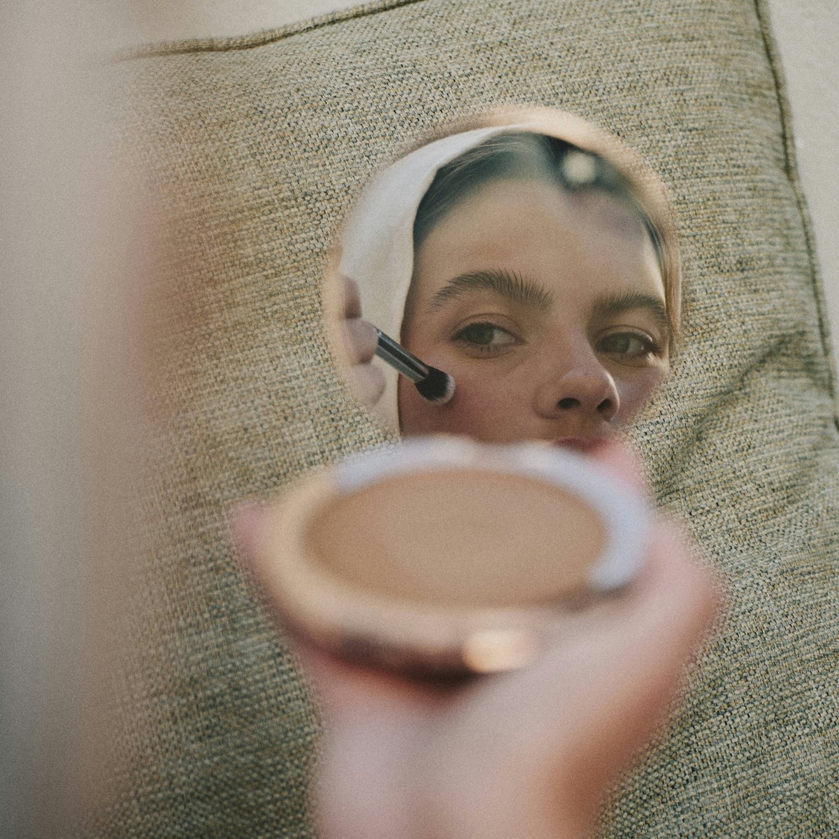 A woman reclined during a facial treatment, holding a compact mirror.