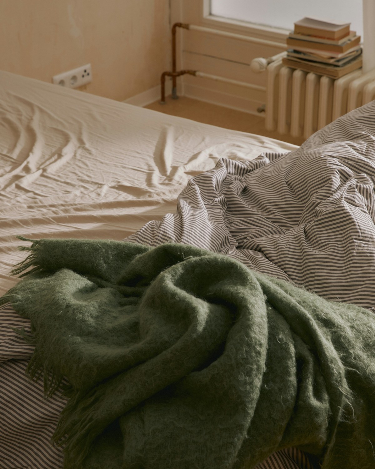 An unmade bed with a green wool throw across it, morning light.