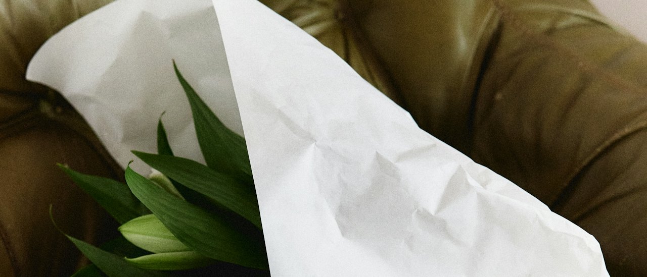 Lilies wrapped in white paper, laid across a worn olive leather chair.